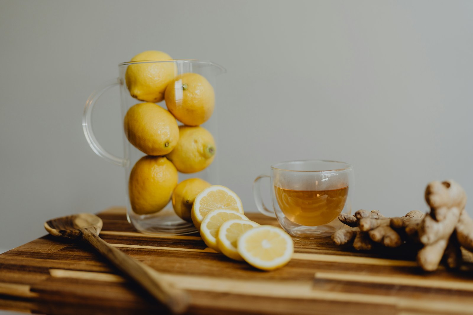 A glass cup of ginger tea beside whole and sliced lemons and fresh ginger root on a wooden board